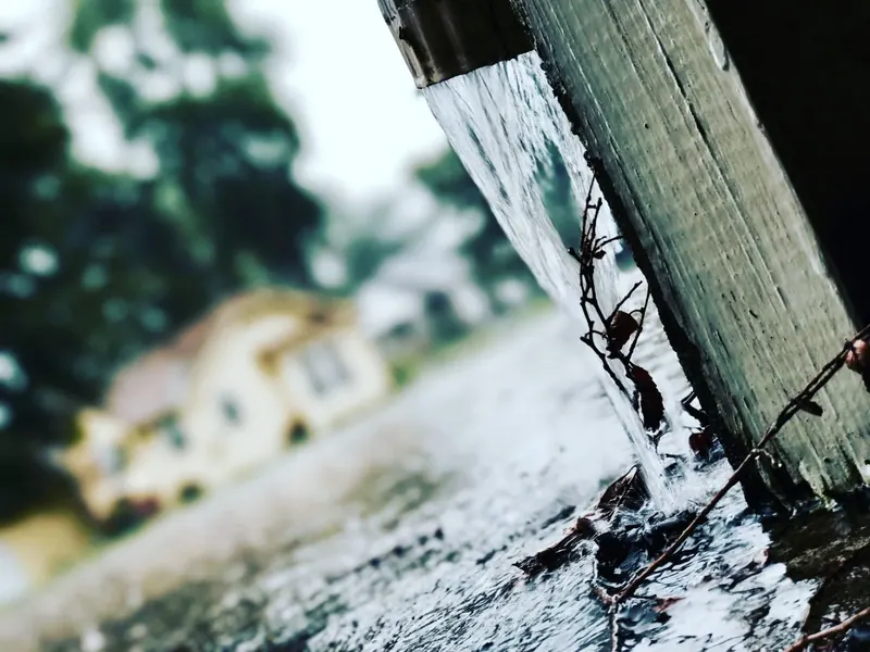 Rainwater pouring off a roof edge where a gutter cannot keep up